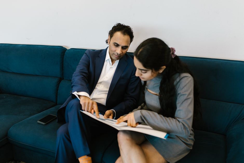 Two colleagues discussing documents on a blue couch in a professional office setting.