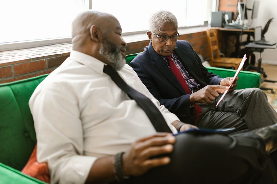 Two mature men engaged in a serious business discussion on a sofa indoors.